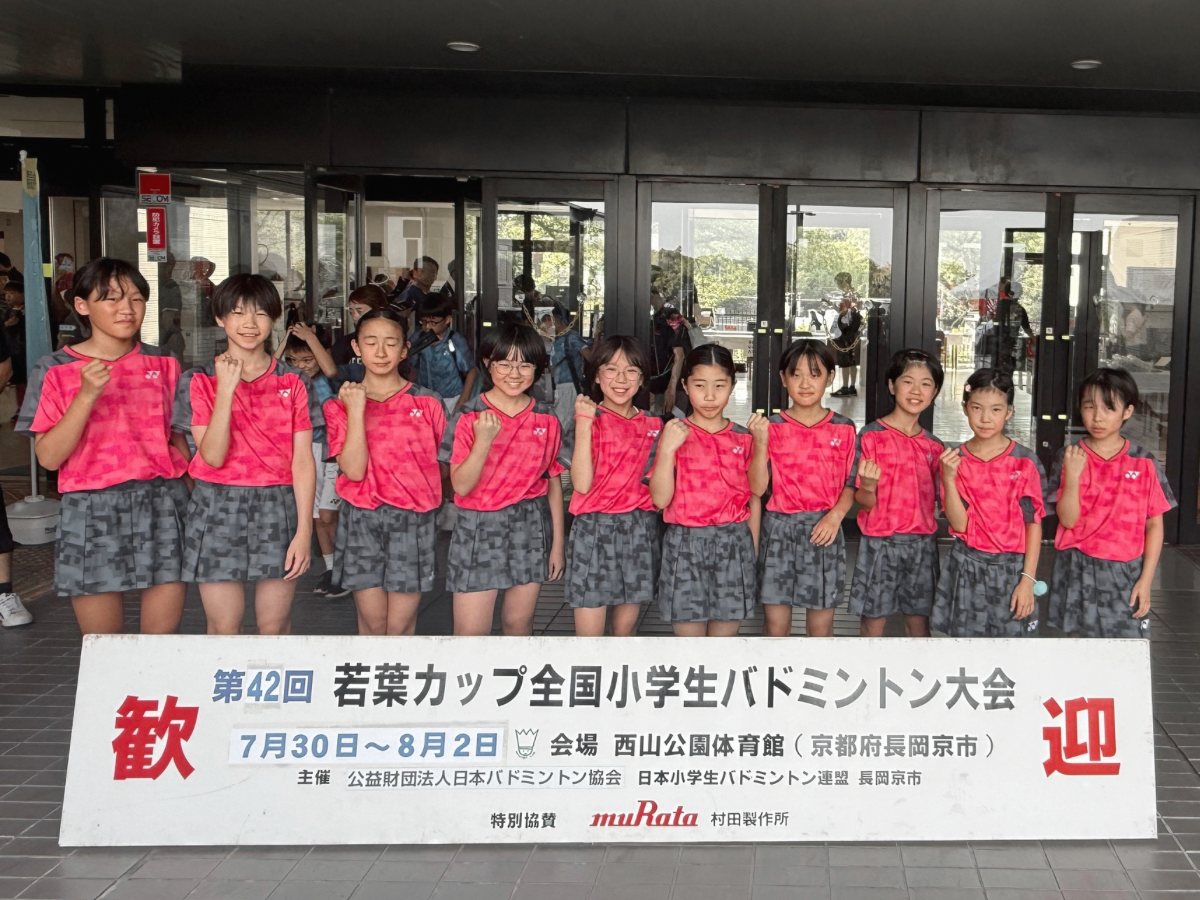 第42回 若葉カップ全国小学生バドミントン大会の看板の前に並ぶ、ピンクのユニフォームの子どもたち